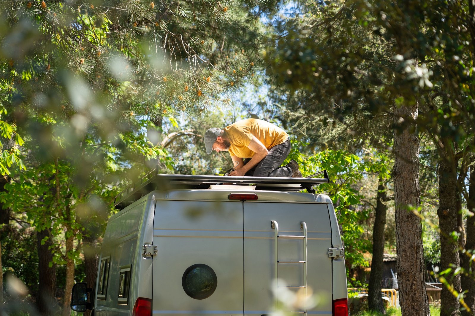 Campervan conversion: man installing solar panel on roof rack in forest